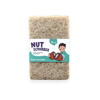 A 2-pack of coconut dish scrubbers wrapped in a white paper label with a cartoon illustration of a boy holding coconuts. The label reads 'NUT SCRUBBER' and 'COCONUT DISH SCRUBBER'.